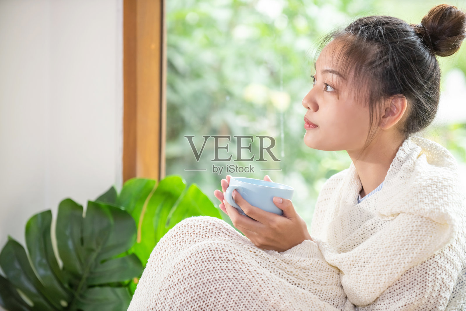 微笑年轻美丽的亚洲女人独自坐在房间里毯子喝热咖啡或茶。美丽的亚洲女孩拿着热咖啡杯，享受放松在家里在清新的早晨照片摄影图片