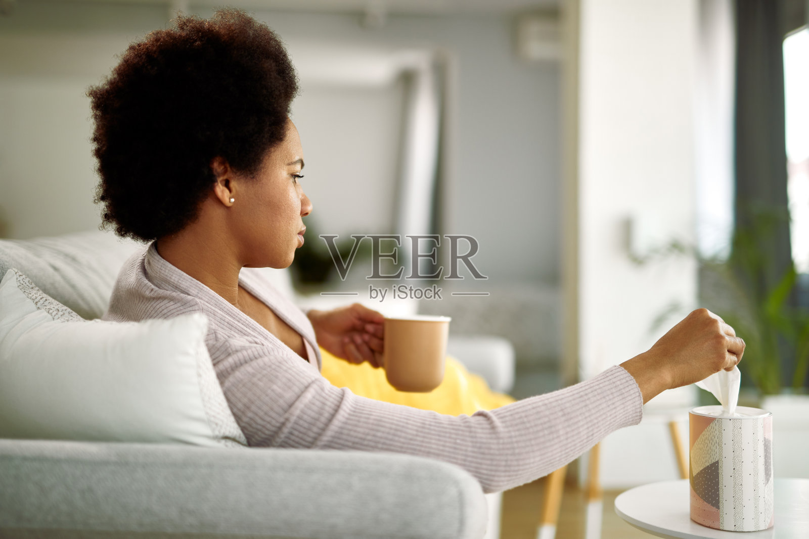 一名黑人妇女在客厅休息时从一个盒子里取出纸巾。照片摄影图片
