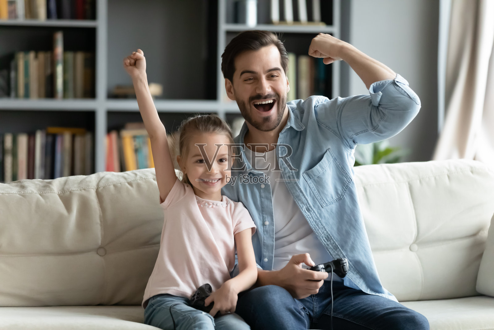 父亲他的小女儿拿着操纵杆玩playstation庆祝成功照片摄影图片