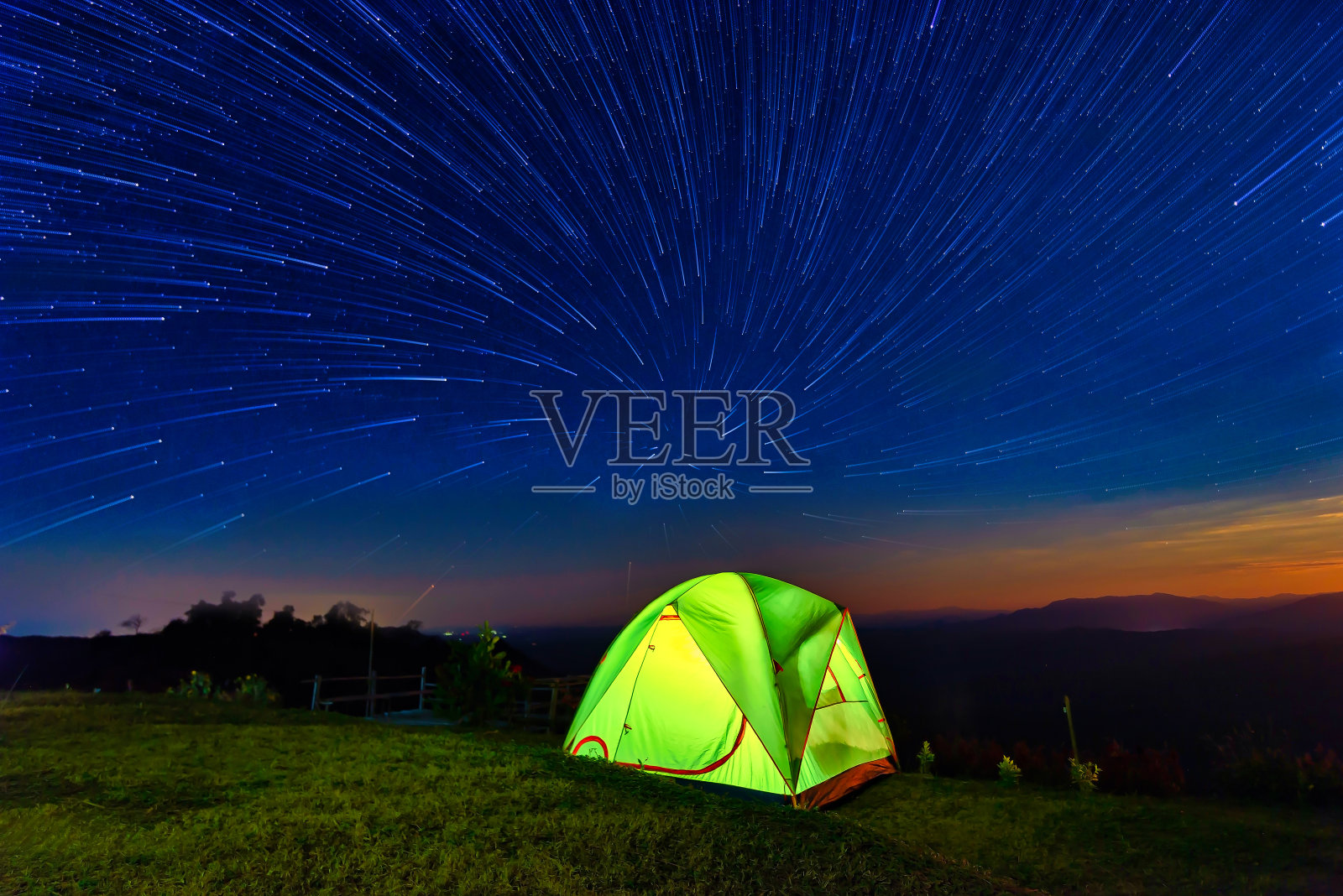 星星在夜晚的山林和发光的露营帐篷上空盘旋照片摄影图片