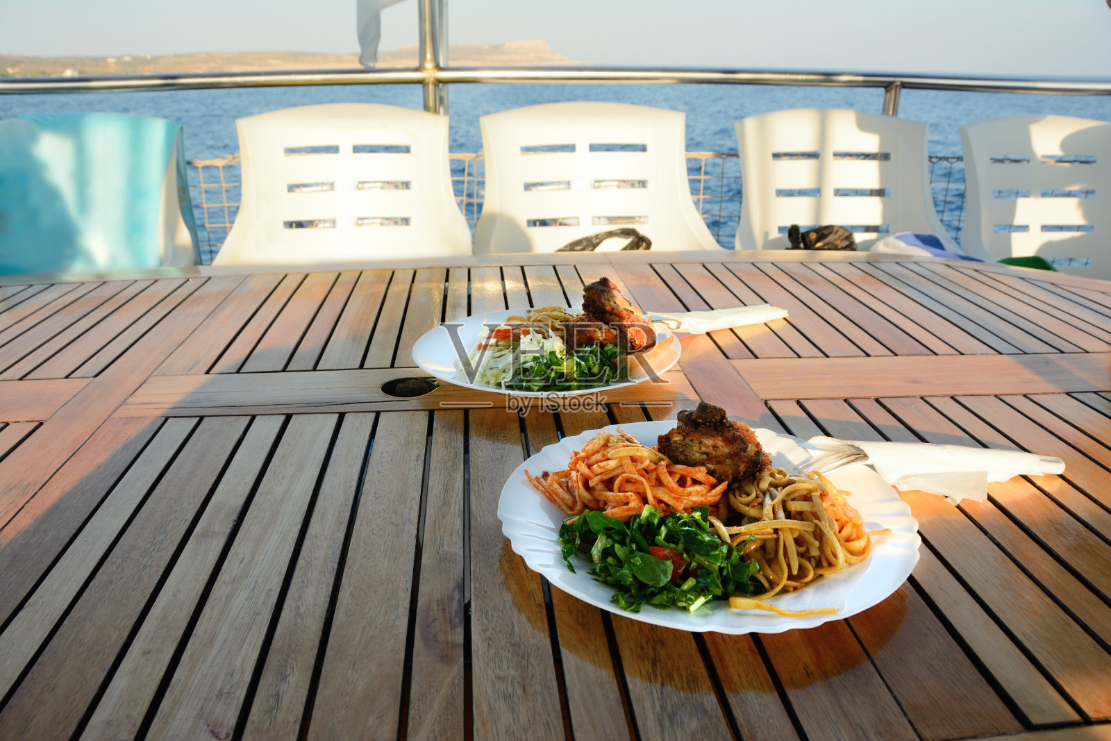 在一艘可以看到海景的游艇上，木桌上摆着一盘盘的食物照片摄影图片