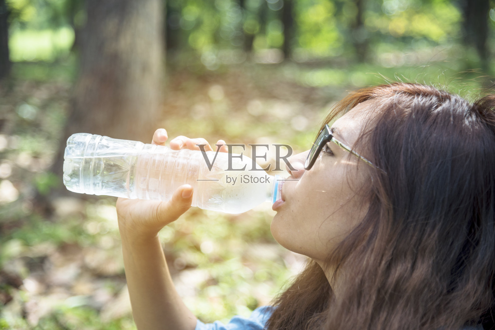 健康的妇女拿着矿泉水在户外镇外的绿色公园微笑，看着镜头与快乐的脸。年轻女子开心的户外生活握着水瓶。照片摄影图片