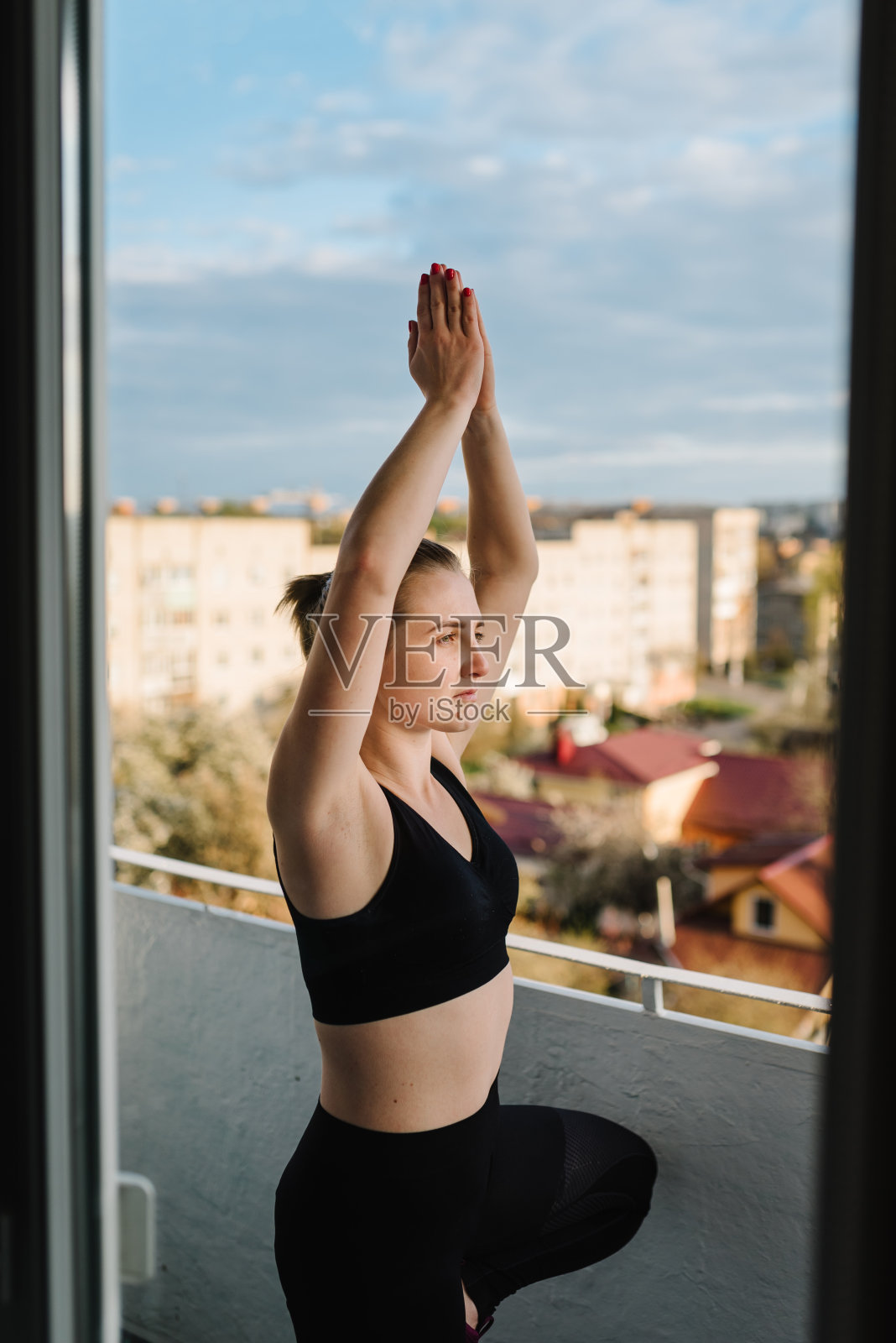 一个女人在阳台上练习瑜伽。Covid-19锁定。运动在家里。一个体育女孩专注于健身与城市景观。呼吸新鲜空气。冷静的概念。冠状病毒留在家里。大流行。照片摄影图片