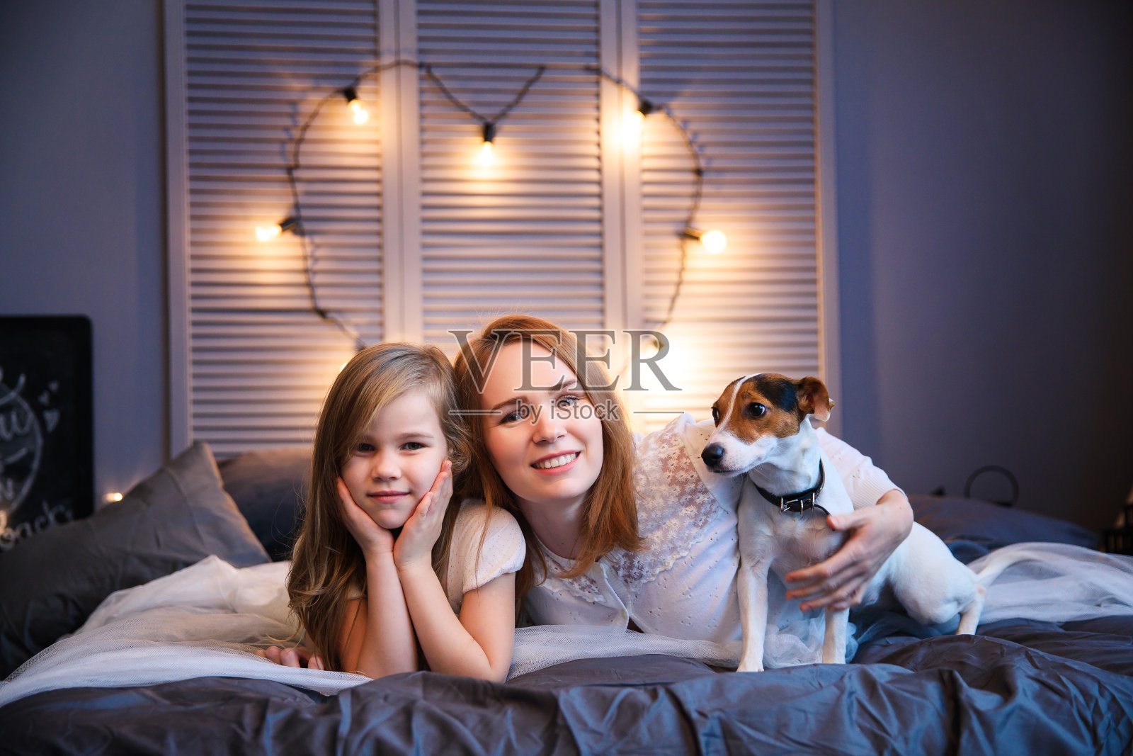 母亲和女儿和狗躺在床上。照片摄影图片