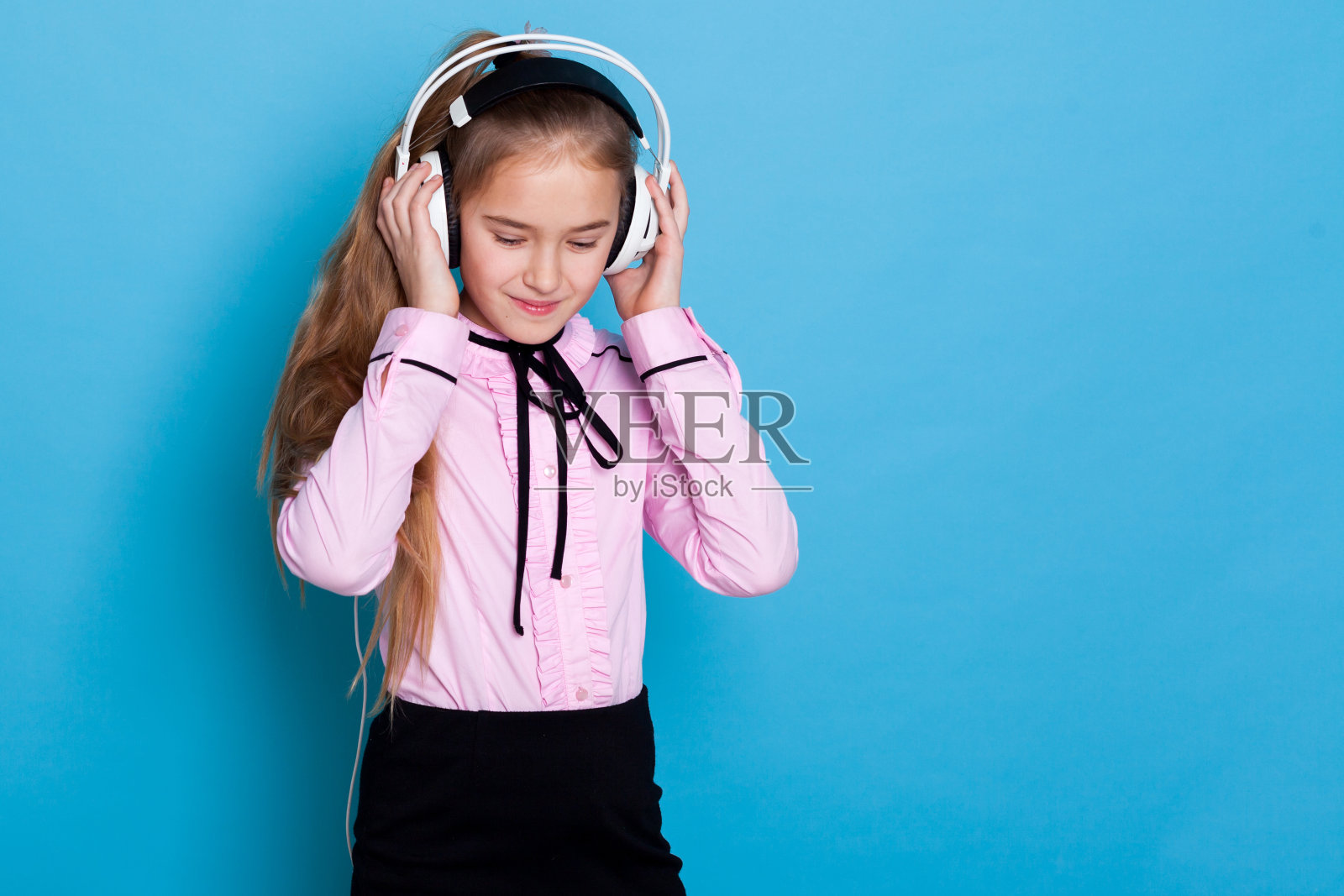 女孩戴着大耳机听音乐，在蓝色背景下跳舞照片摄影图片