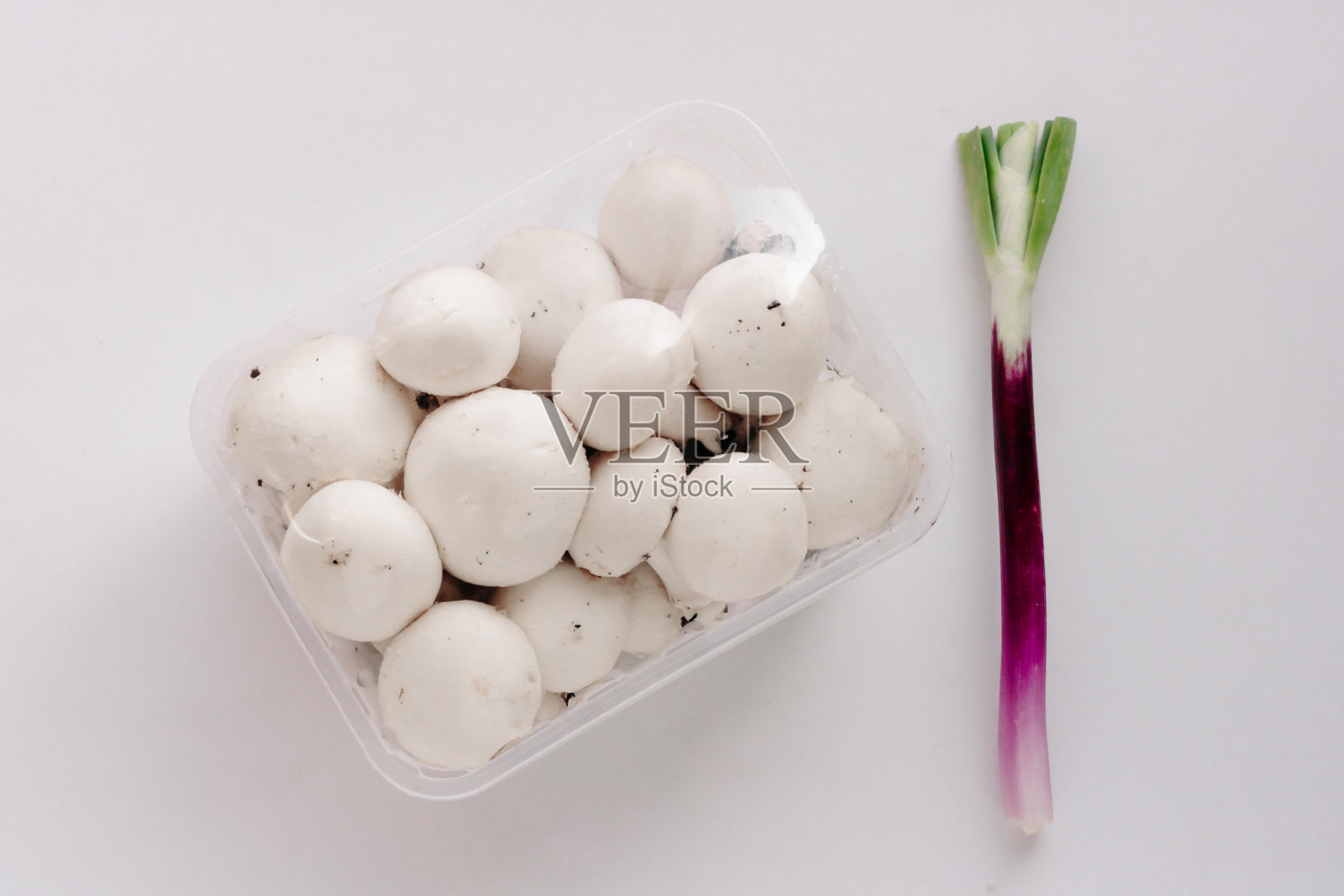 新鲜的蘑菇、塑料包装的白色香椿和白色背景的大葱(青葱或大葱)。新鲜食品塑料包装回收与环境生态问题的概念。前视图。照片摄影图片