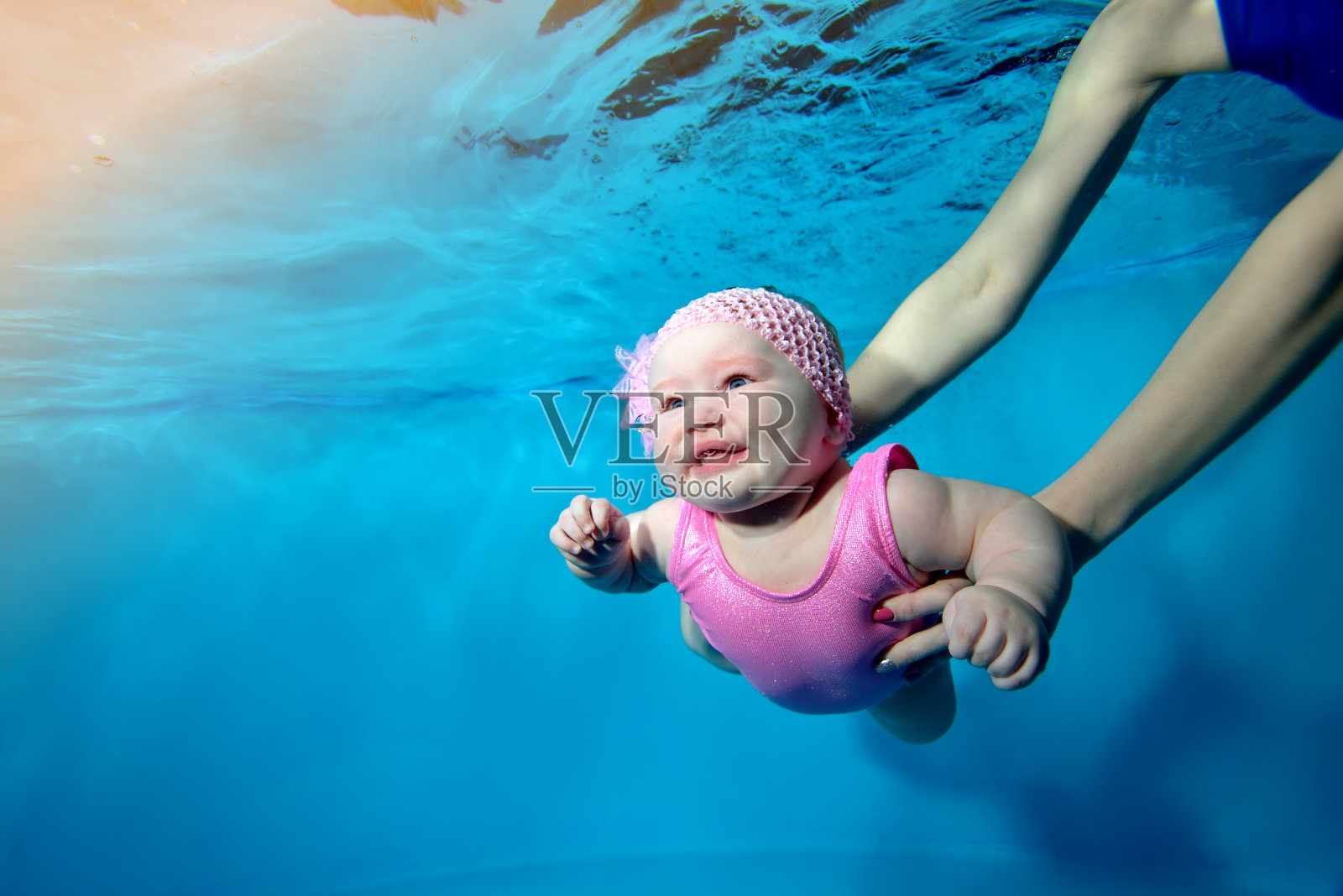一个微笑的小女孩在儿童游泳池的水下游泳的特写镜头，她的母亲用她的胳膊支持她。的概念。数码照片。水平方向。照片摄影图片