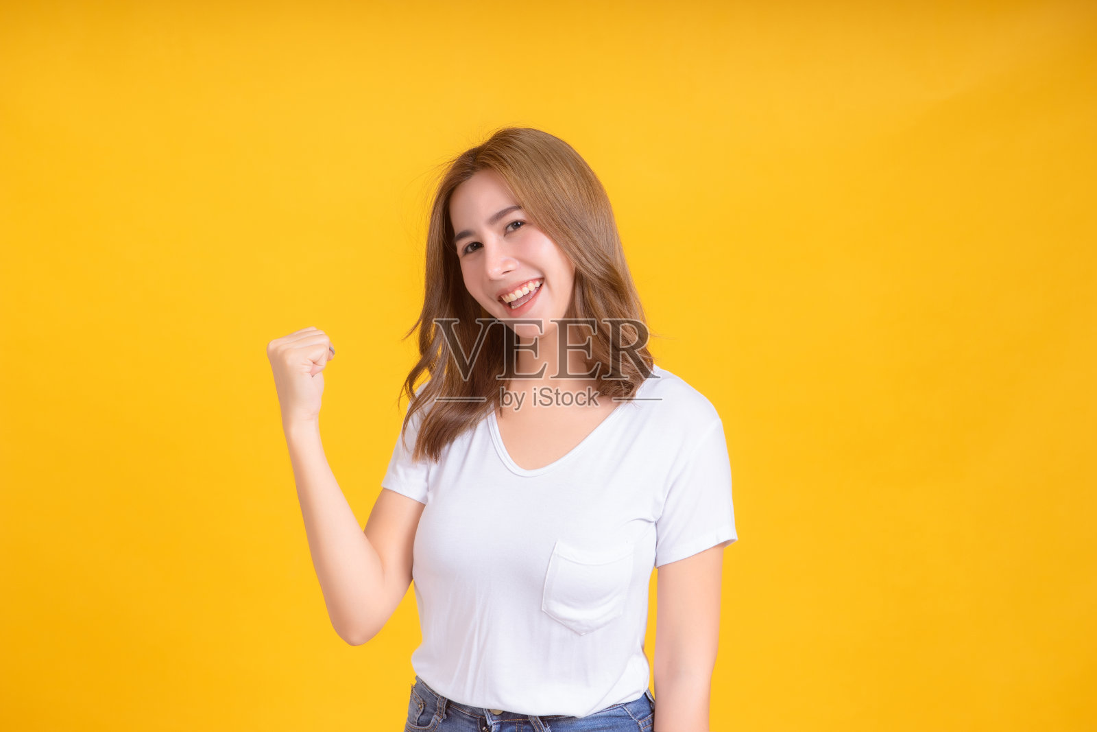 肖像快乐的年轻亚洲妇女微笑举起拳头幸运积极的情绪在白色t恤，黄色背景孤立的工作室拍摄和复制空间。照片摄影图片