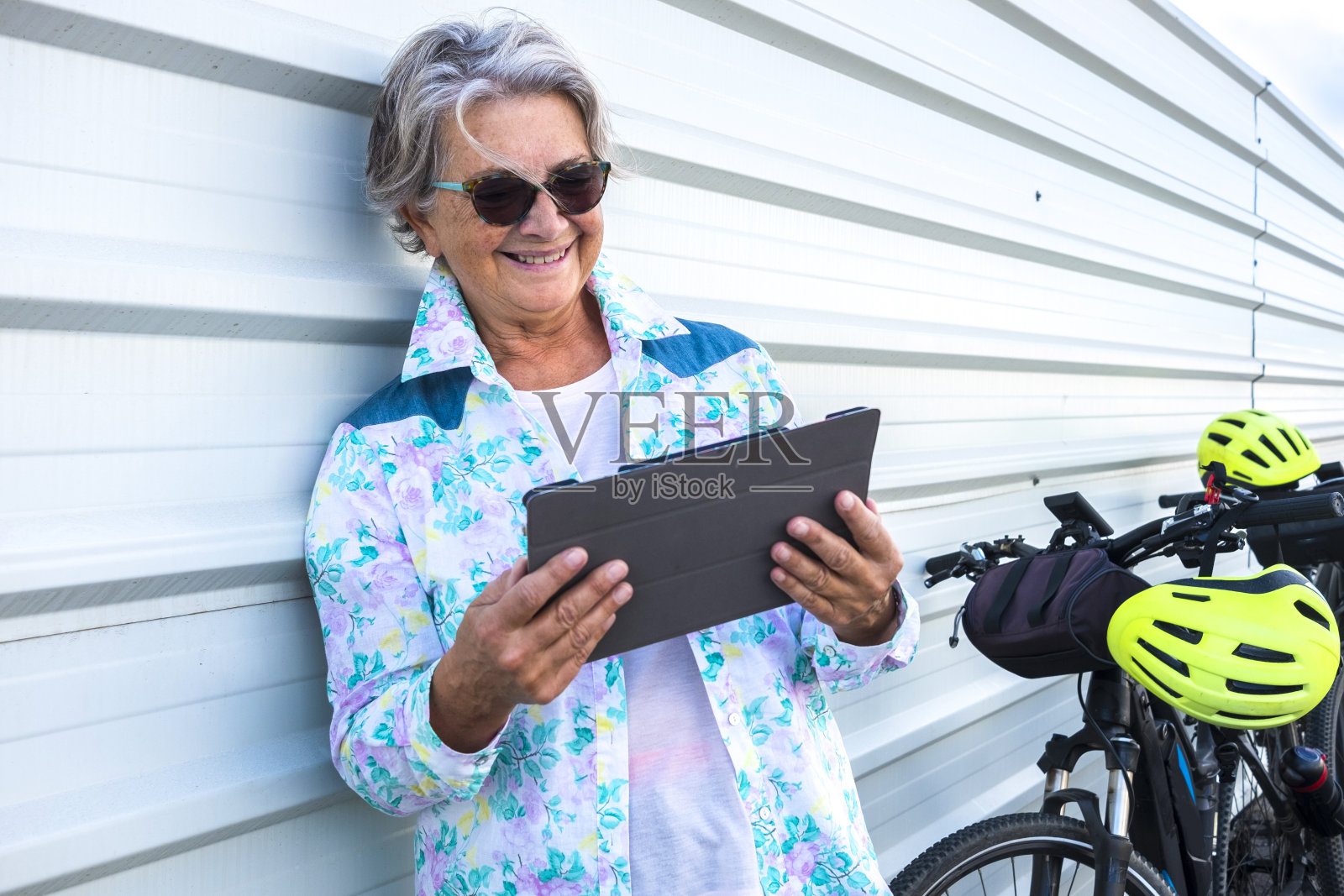 快乐的老年妇女停止驾驶电动自行车，在她的平板电脑上阅读新闻。积极的退休人员和健康的生活方式的概念照片摄影图片