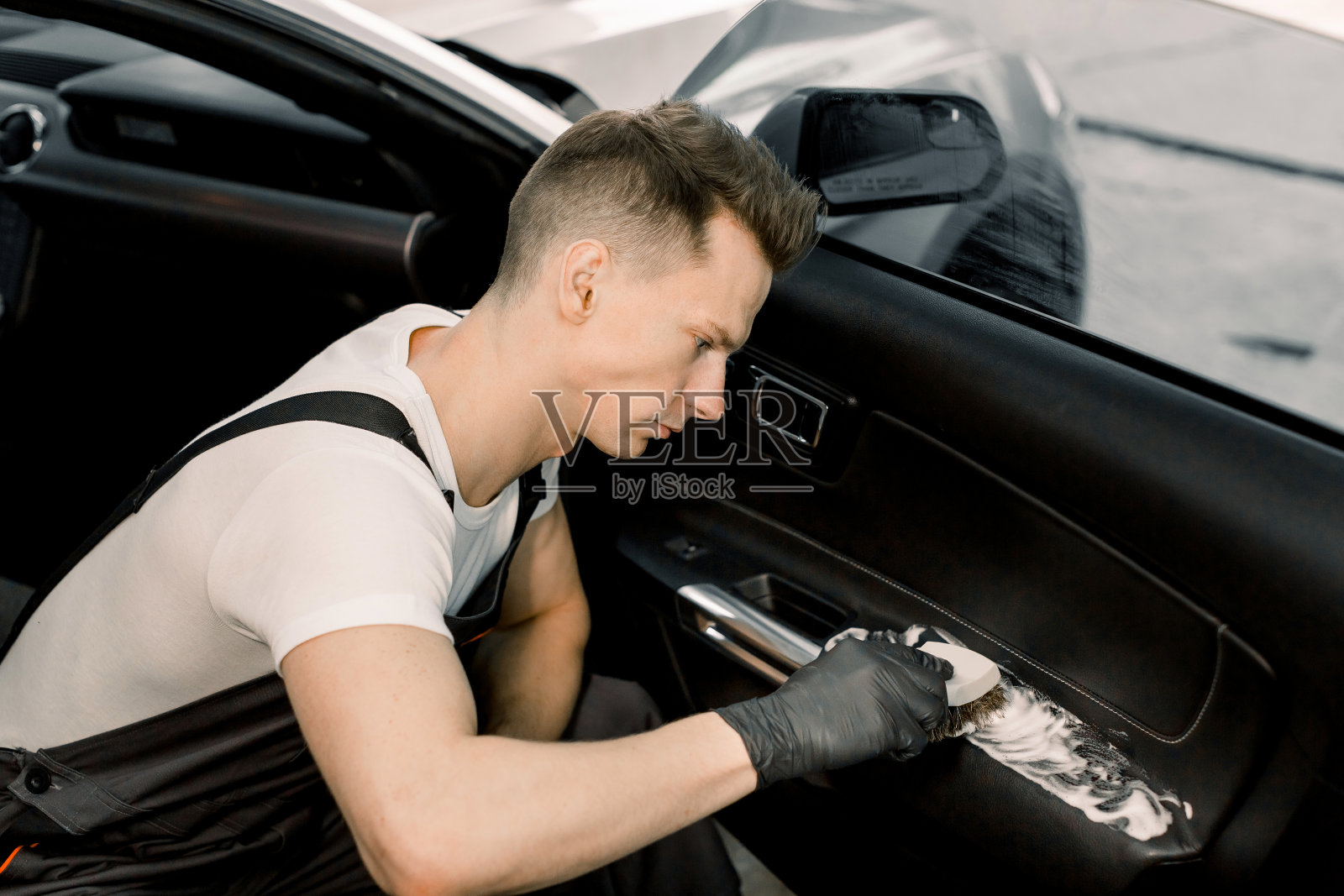 帅气的年轻人，专业汽车装饰车间的工人，正在用泡沫软刷清洗车门内部。汽车清洗和细节概念照片摄影图片