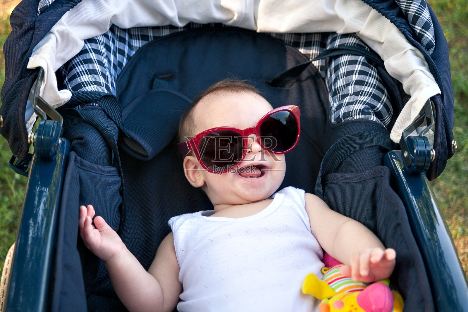 小婴儿在婴儿车里戴着有趣的大墨镜，有趣的婴儿笑着戴着太阳镜，夏天阳光灿烂照片摄影图片