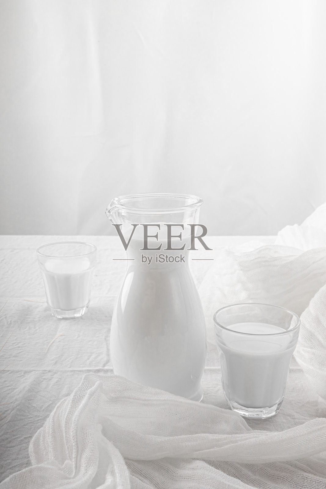 牛奶在一个罐子和玻璃杯在白色的背景。桌布。花。副本的空间。照片摄影图片