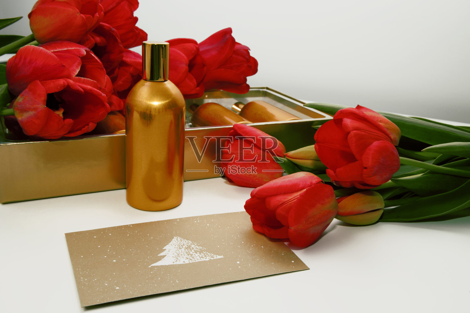 信封的表面是一幅云杉的画，里面有一个金色的瓶子和红色的郁金香。照片摄影图片