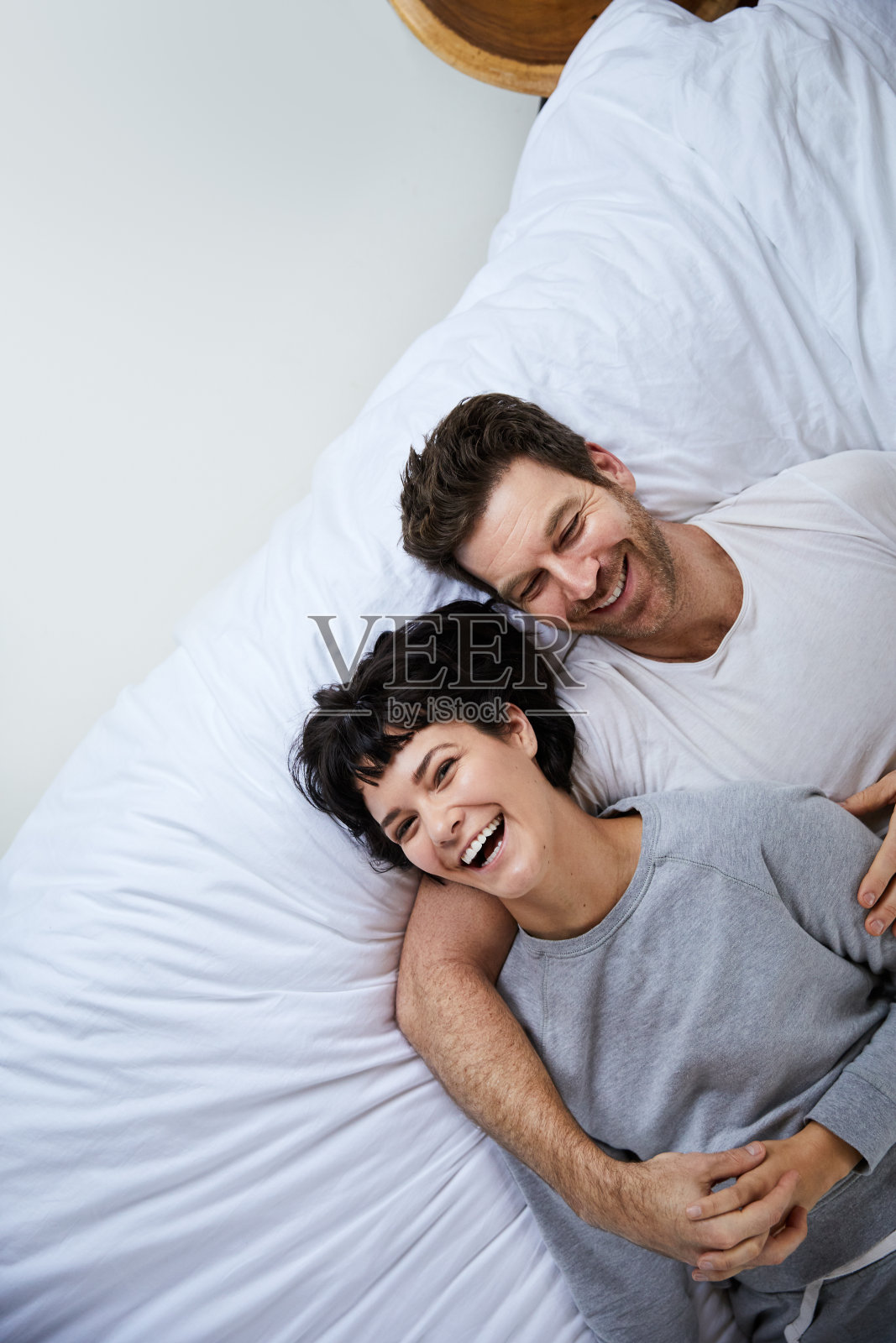 清晨，一对笑嘻嘻的年轻夫妇躺在床上照片摄影图片