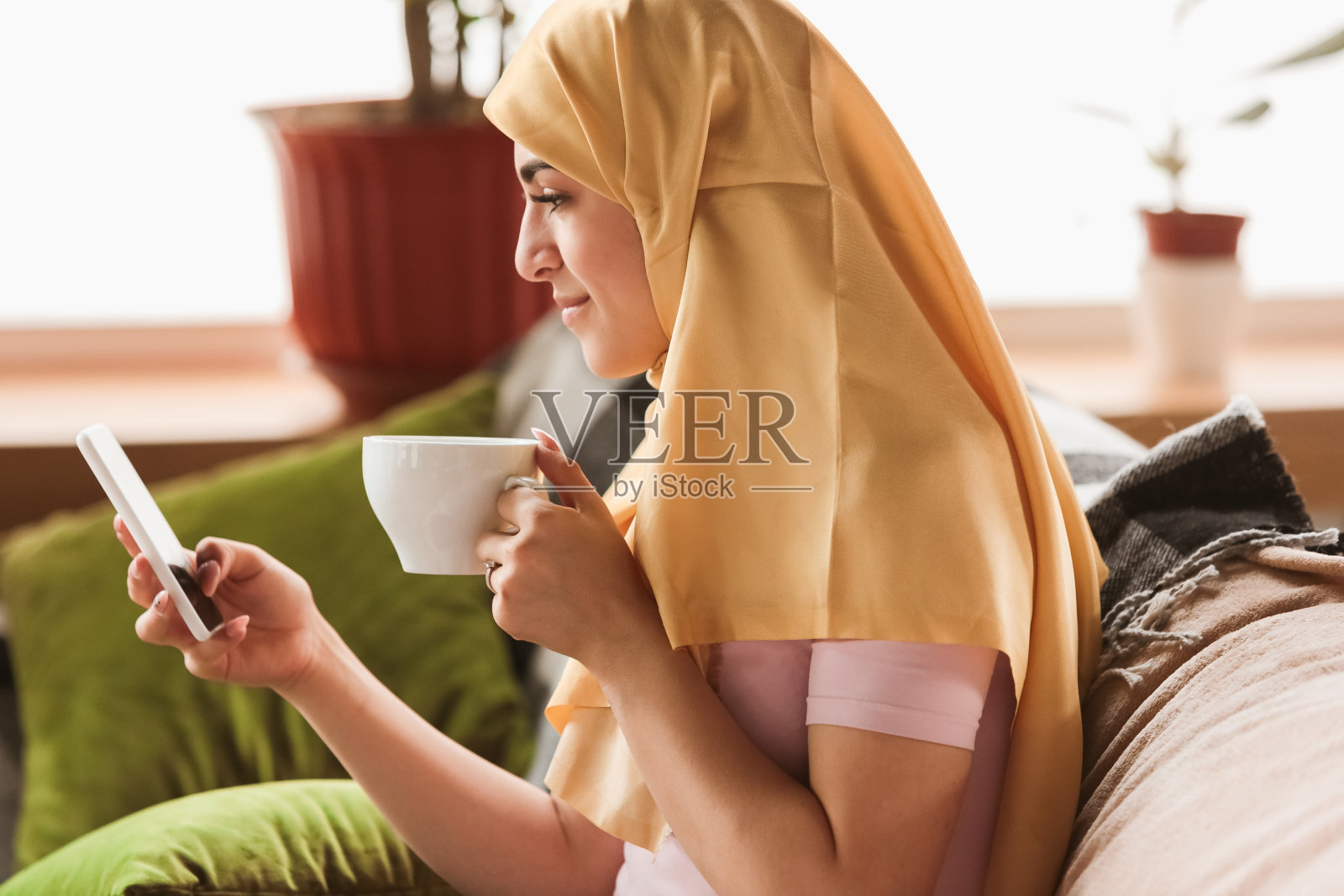 一名年轻漂亮的穆斯林女子在家中隔离和自我隔离，使用智能手机自拍或视频通话，在线上课，购物照片摄影图片