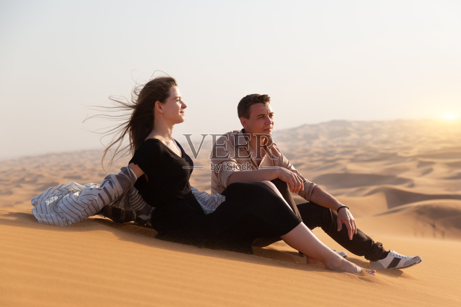 一男一女正坐在沙漠里滚烫的沙滩上。照片摄影图片
