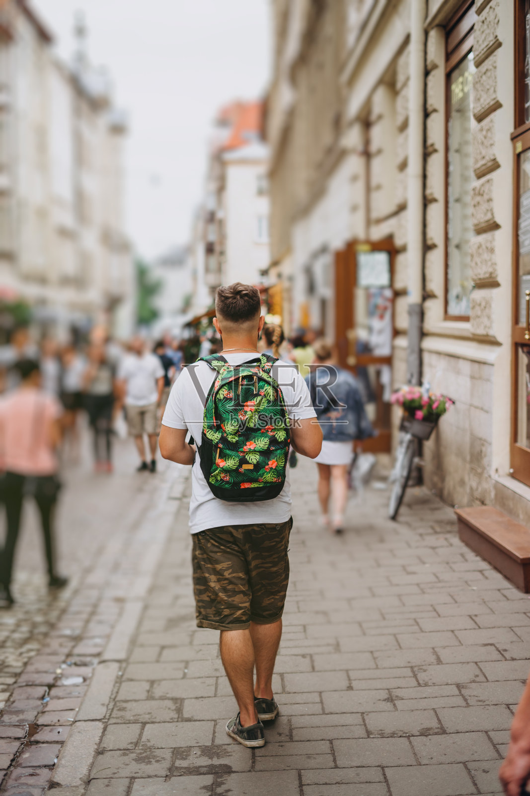 一个男人背着背包在夏天的城市旅游。一个年轻人在一个阳光明媚的日子走在城市里。穿着短裤背着彩色背包的运动男。照片摄影图片