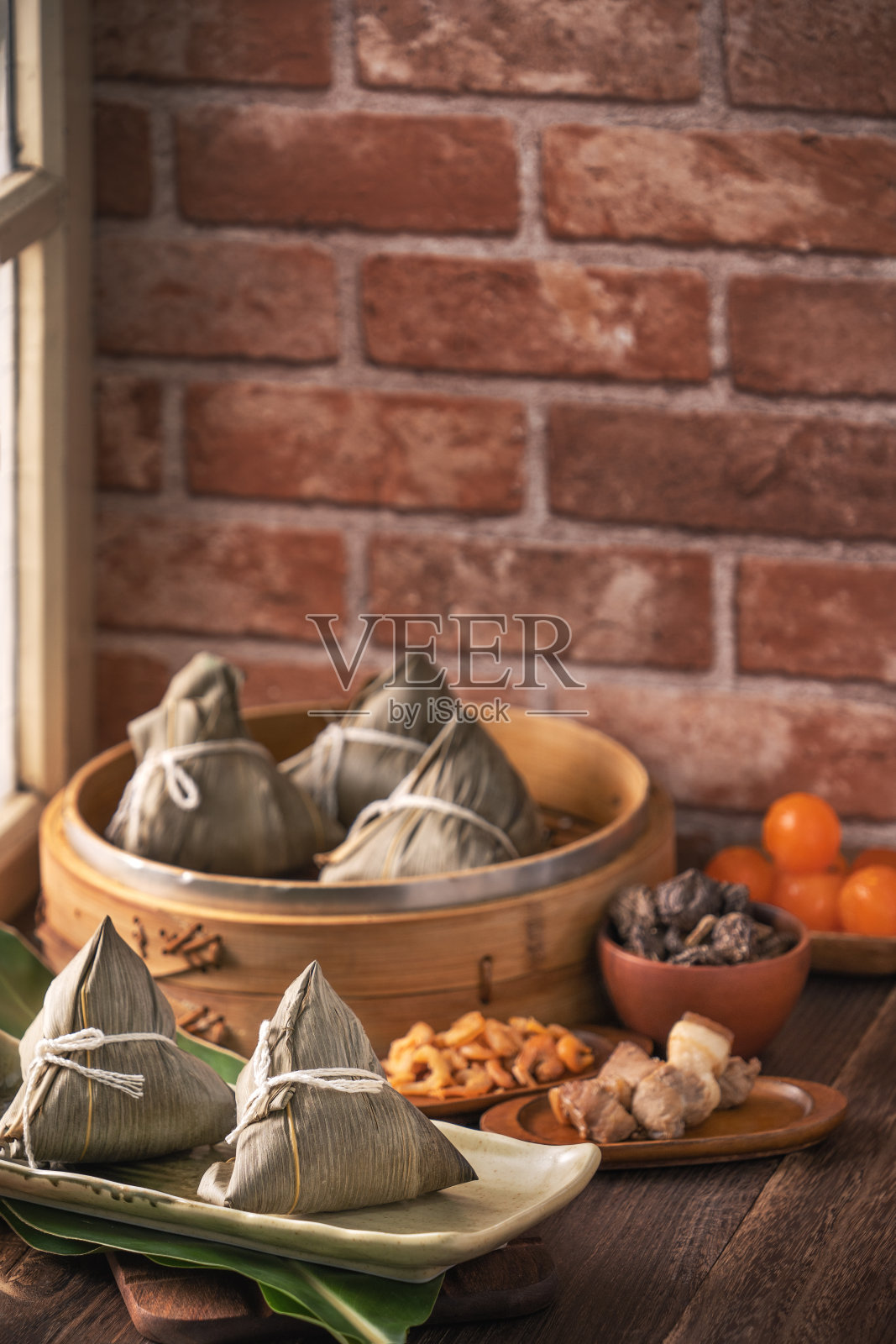 粽子——粽子在蒸笼上用红砖砌成的木桌上，窗户背景为家里的端午观念。照片摄影图片