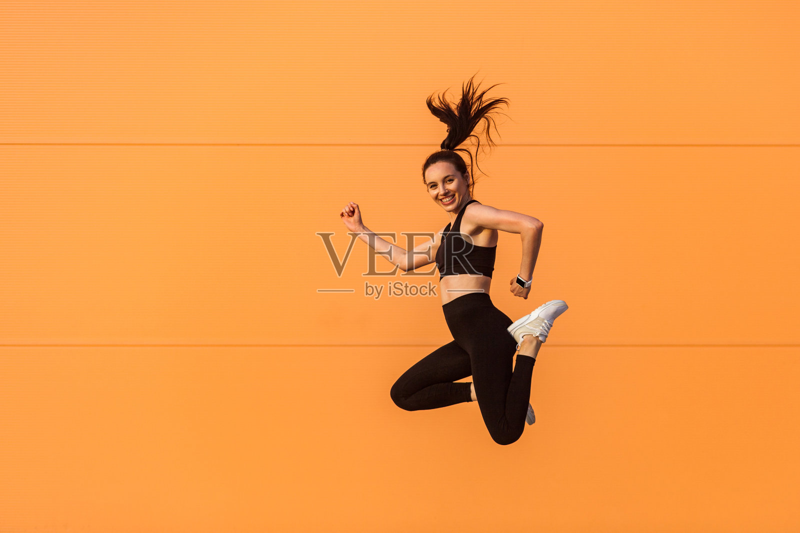 快乐活泼生动的女孩穿着紧身运动服在空中跳跃，飞扬着笑容，充满活力，健康的运动生活方式照片摄影图片