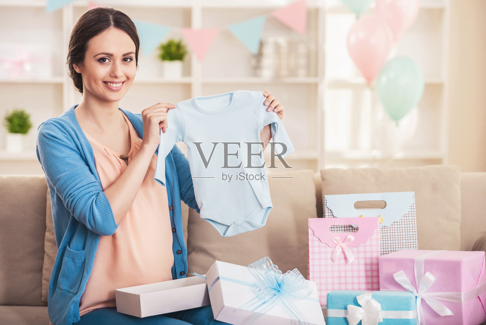 微笑孕妇与蓝色婴儿连体衣。照片摄影图片