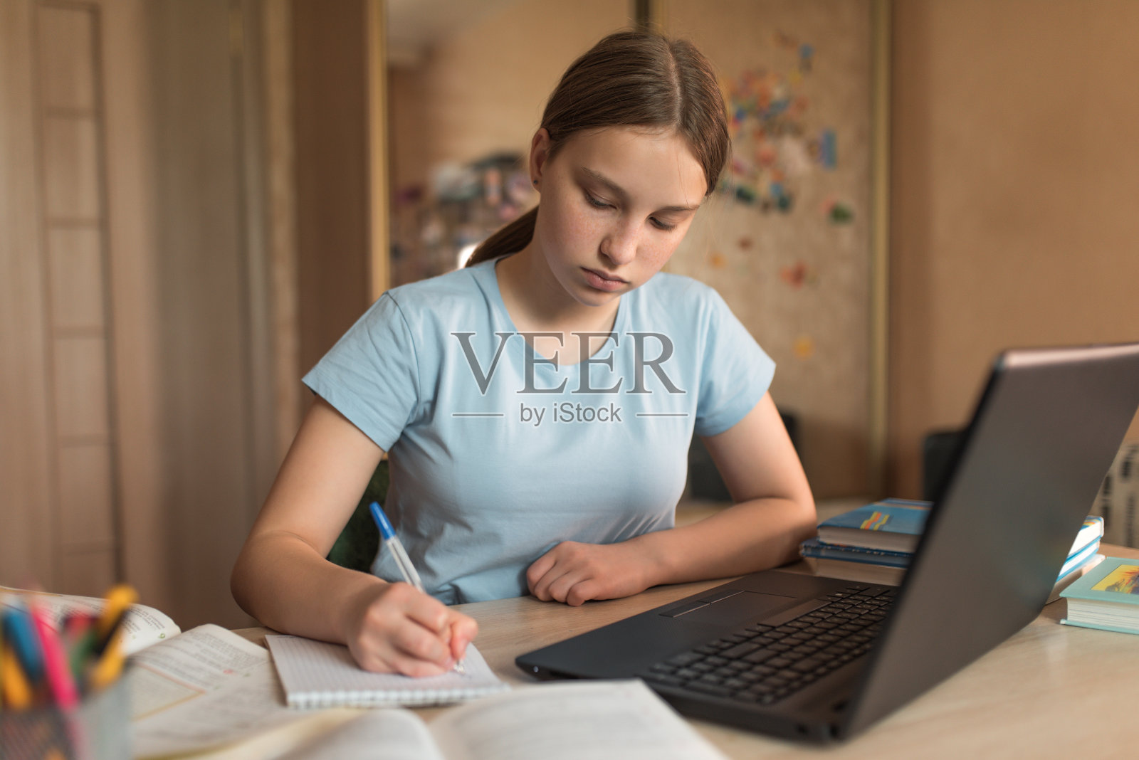 12-15岁的少女，在家里用笔写字，写黑板课，上网学习，用笔记本电脑上网。隔离期间进行远程教育，待在家里。照片摄影图片