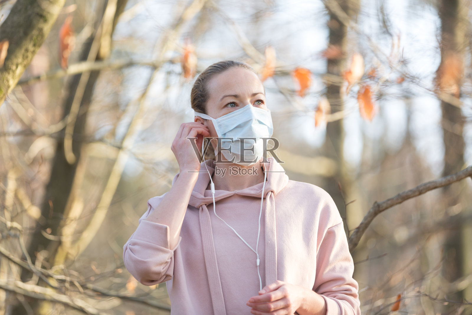 在公园里散步、放松和听音乐时，穿着医疗保护面罩的白人运动妇女的肖像。冠状病毒(Covid-19)正在全球蔓延照片摄影图片