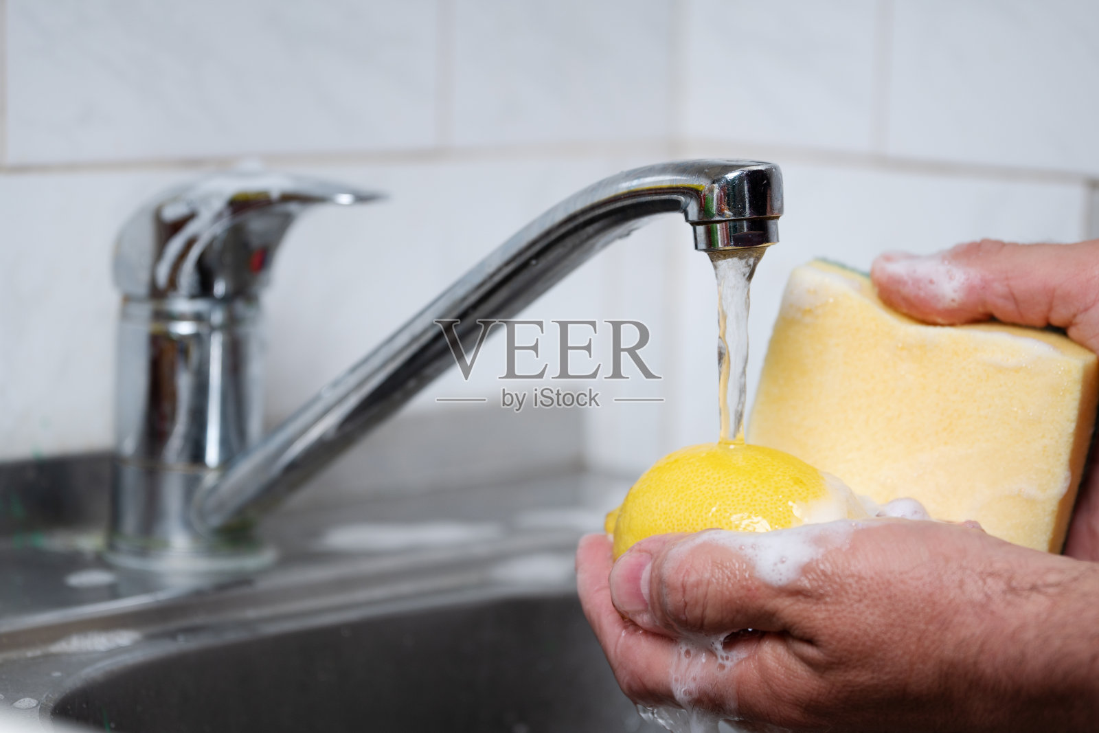 男性用海绵蘸着肥皂泡沫在厨房水槽里用柠檬洗手照片摄影图片