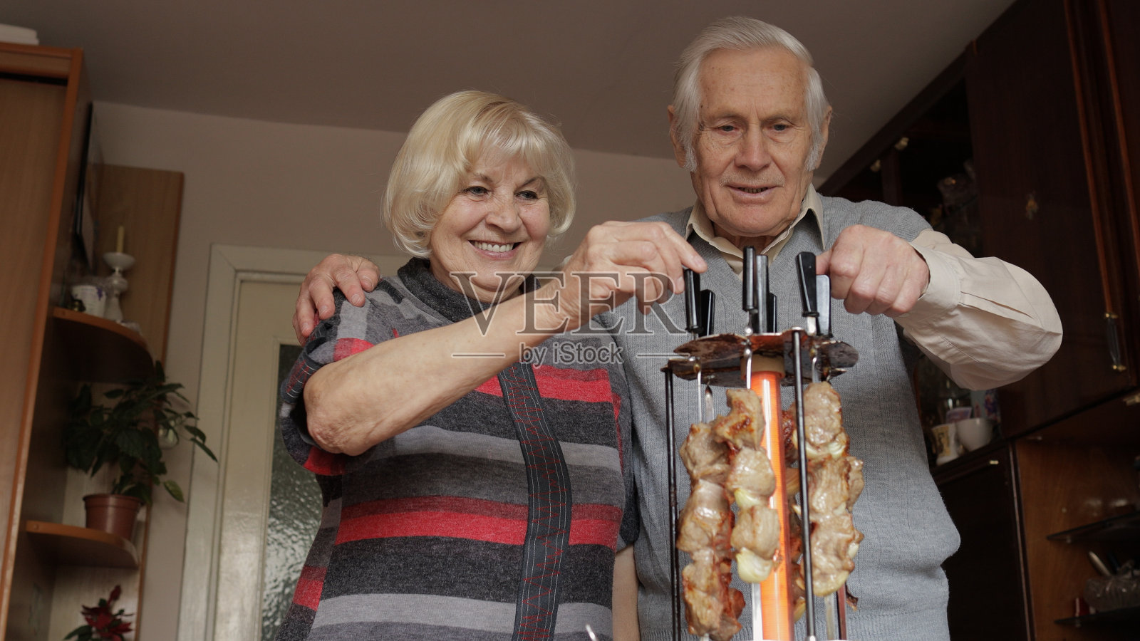 快乐的老祖父母夫妇在家里用电烤架烹饪烧烤照片摄影图片