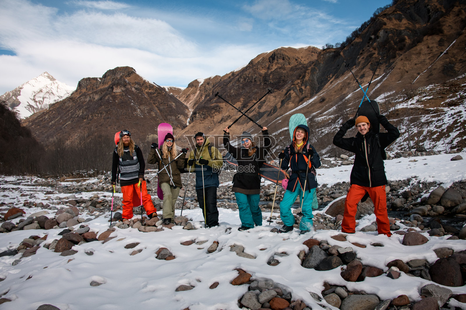 一群快乐的游客带着滑雪装备沿着山河行走。照片摄影图片
