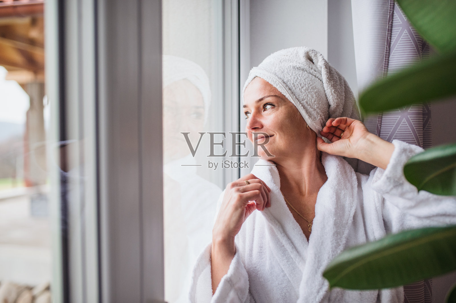 一个穿着浴袍和毛巾头站在室内的女人的肖像。照片摄影图片
