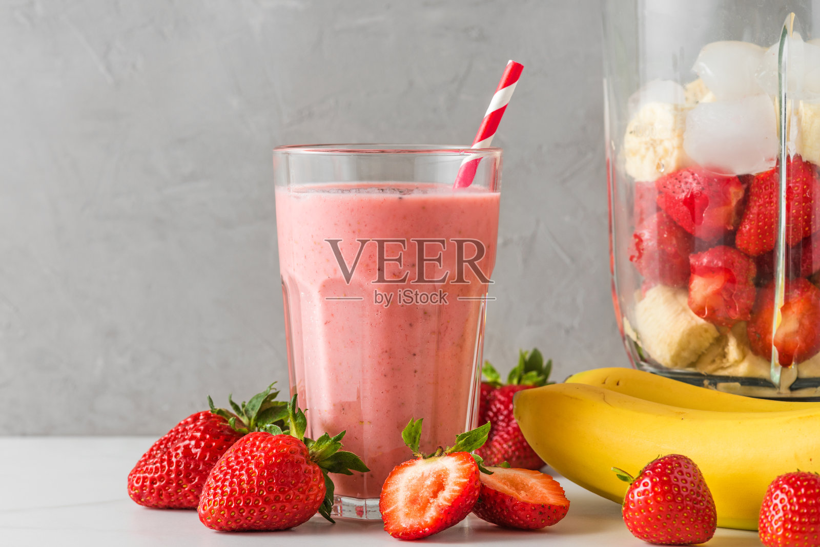 一杯健康的冰沙或奶昔，用草莓，香蕉，杏仁牛奶和搅拌机和吸管制成照片摄影图片
