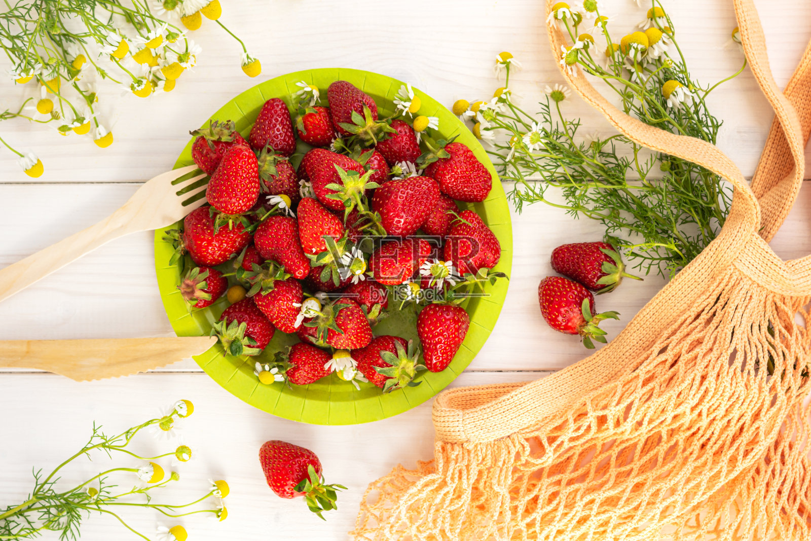 草莓与雏菊俯视图。绿色盘子里放着红浆果，还有一束雏菊照片摄影图片