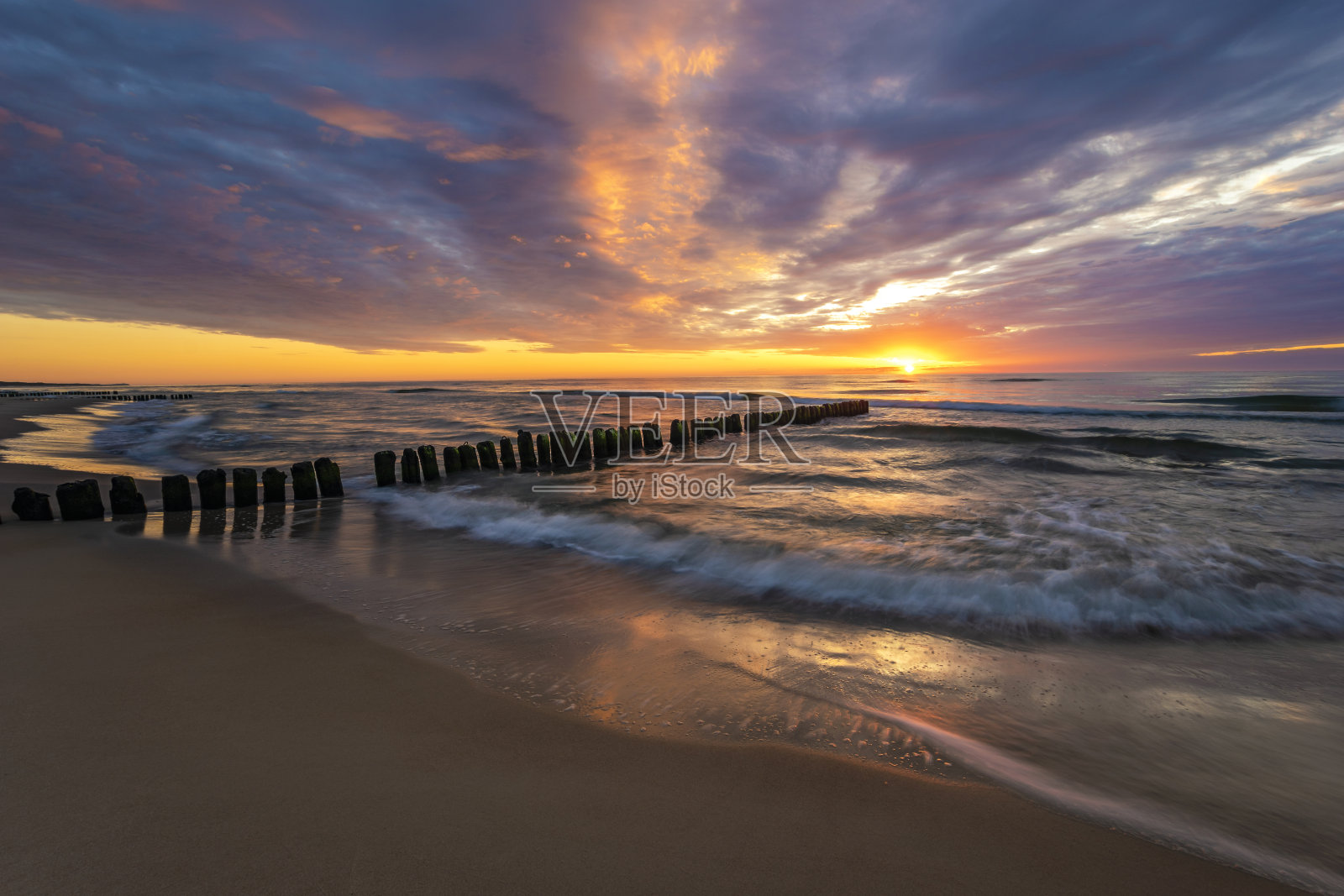 美丽的波罗的海日落，海浪冲刷着古老的木制防波堤照片摄影图片