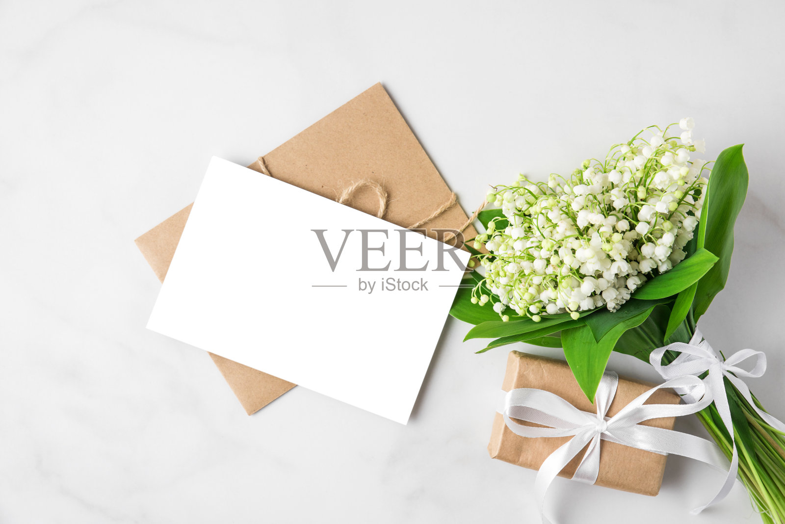 空白贺卡与山谷百合花束和礼盒在白色的背景。模拟。平躺照片摄影图片