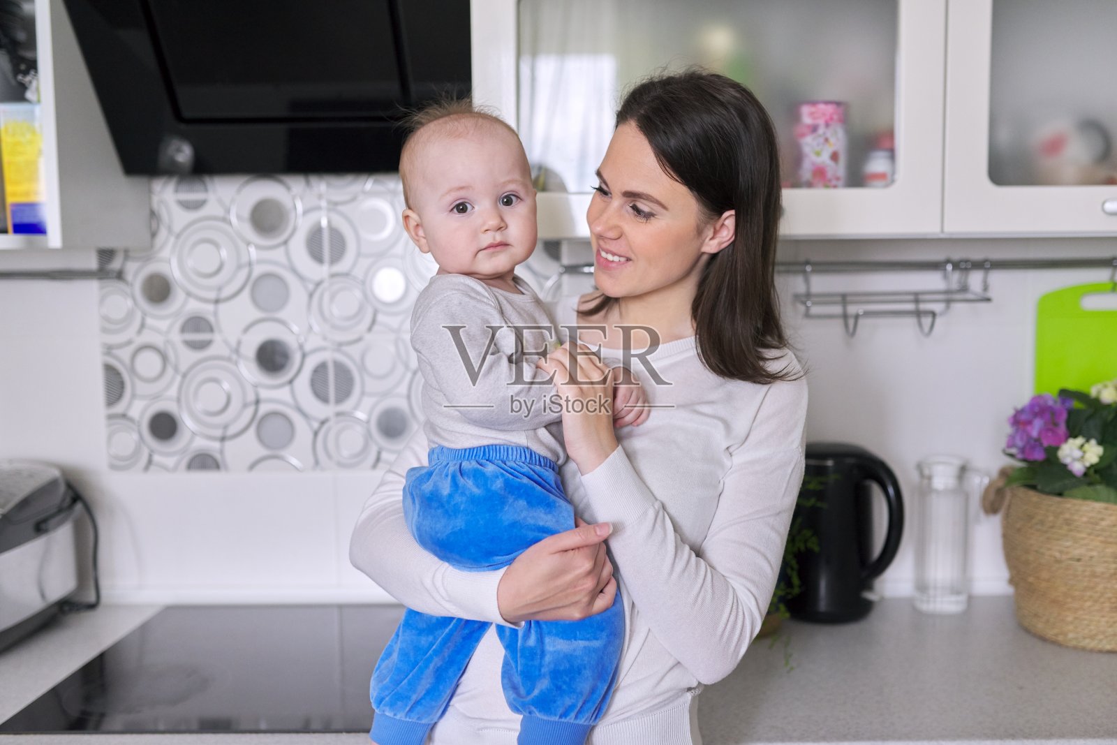 微笑的妇女抱着1岁的婴儿在厨房照片摄影图片