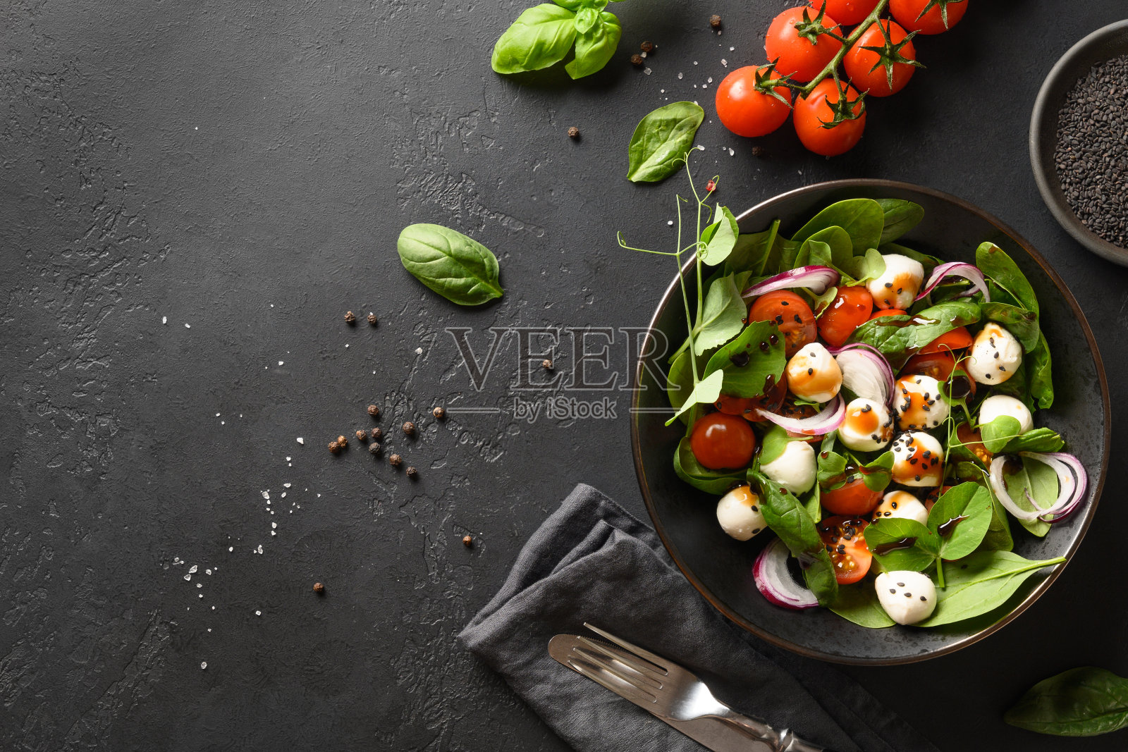以菠菜、圣女果、洋葱和马苏里拉奶酪为背景的黑石头沙拉。前视图。照片摄影图片
