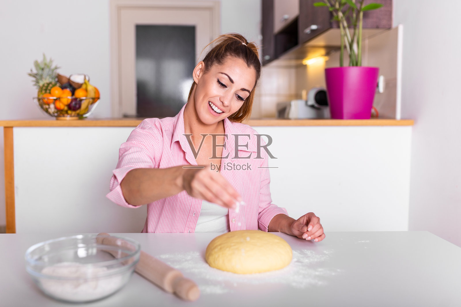 快乐的女人在家里的厨房揉面。年轻快乐的妇女在做面包，家庭主妇在厨房做饭照片摄影图片