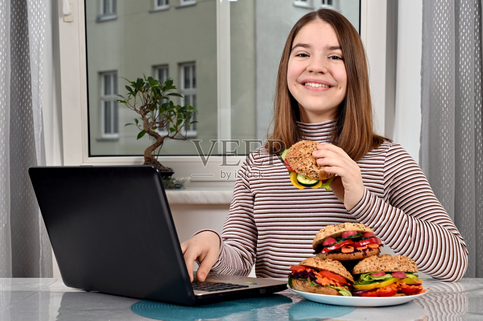 十几岁的女孩用笔记本电脑在家吃素食三明治照片摄影图片