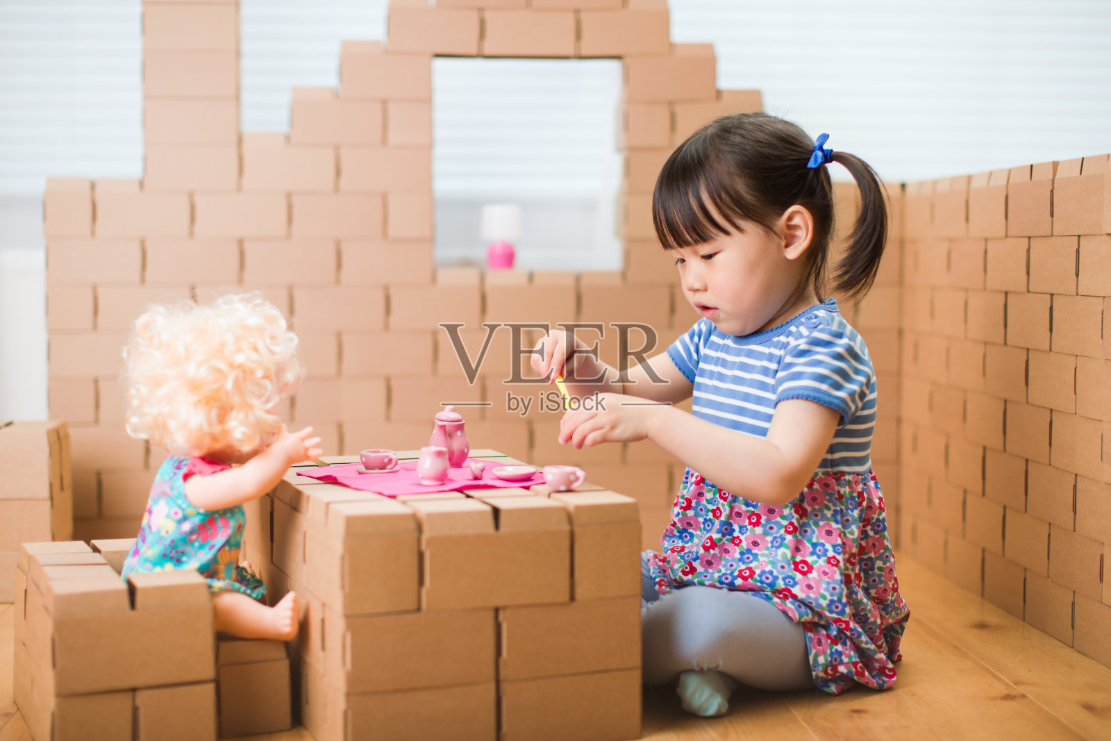 蹒跚学步的小女孩假装在纸板积木房子里玩婴儿护理照片摄影图片