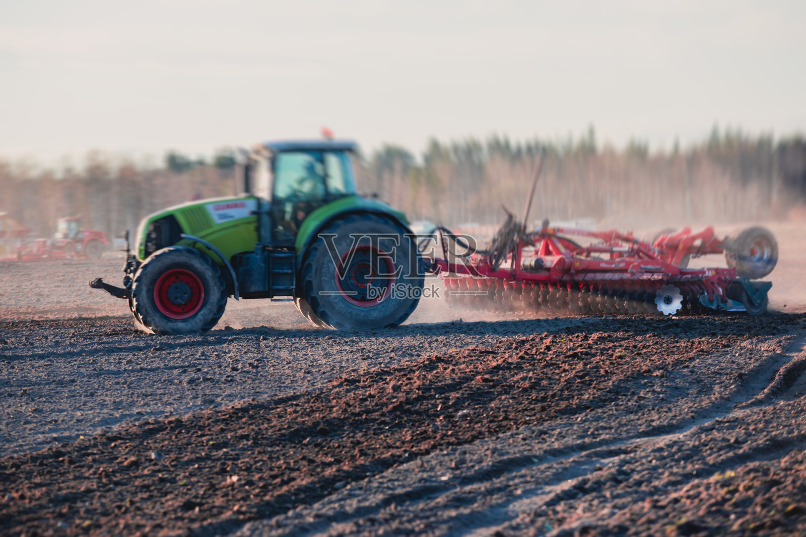 拖拉机用圆盘耙系统耙耕地，耙和准备土壤的过程，拖拉机在日落时在田里播种作物，农业概念，耙机在工作照片摄影图片