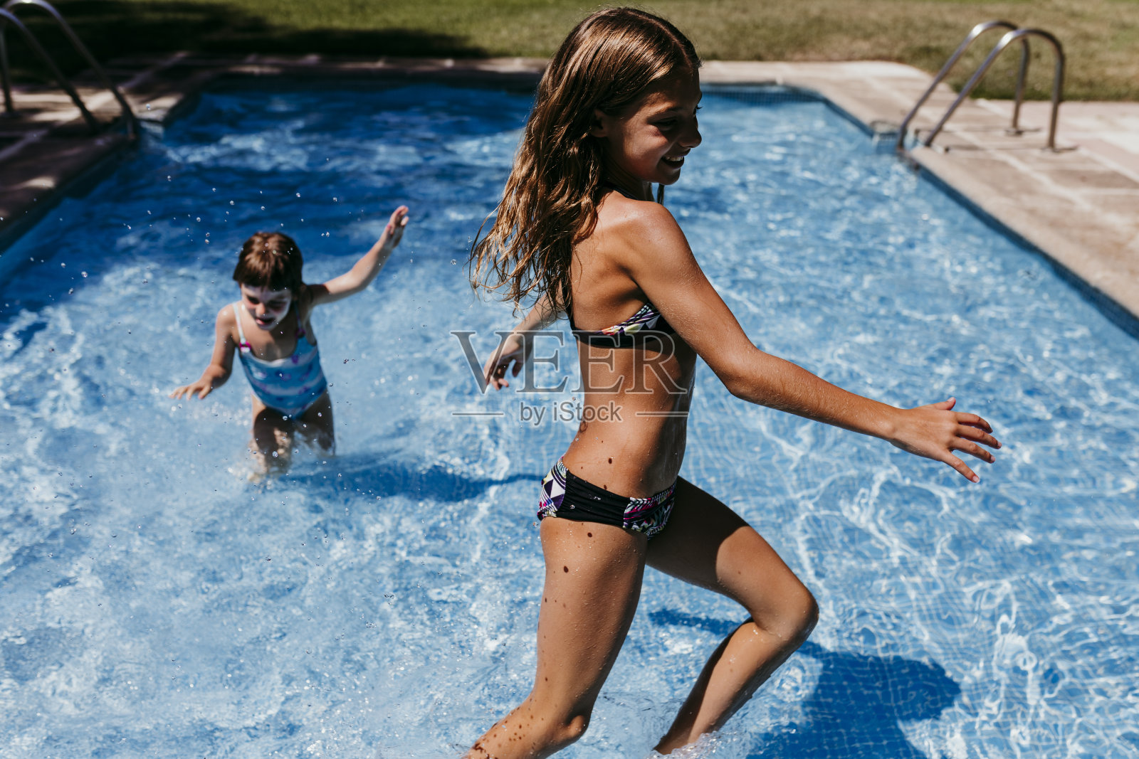两个漂亮的姐妹孩子在游泳池里玩耍，跑步，在户外玩耍。夏季和生活方式的概念照片摄影图片