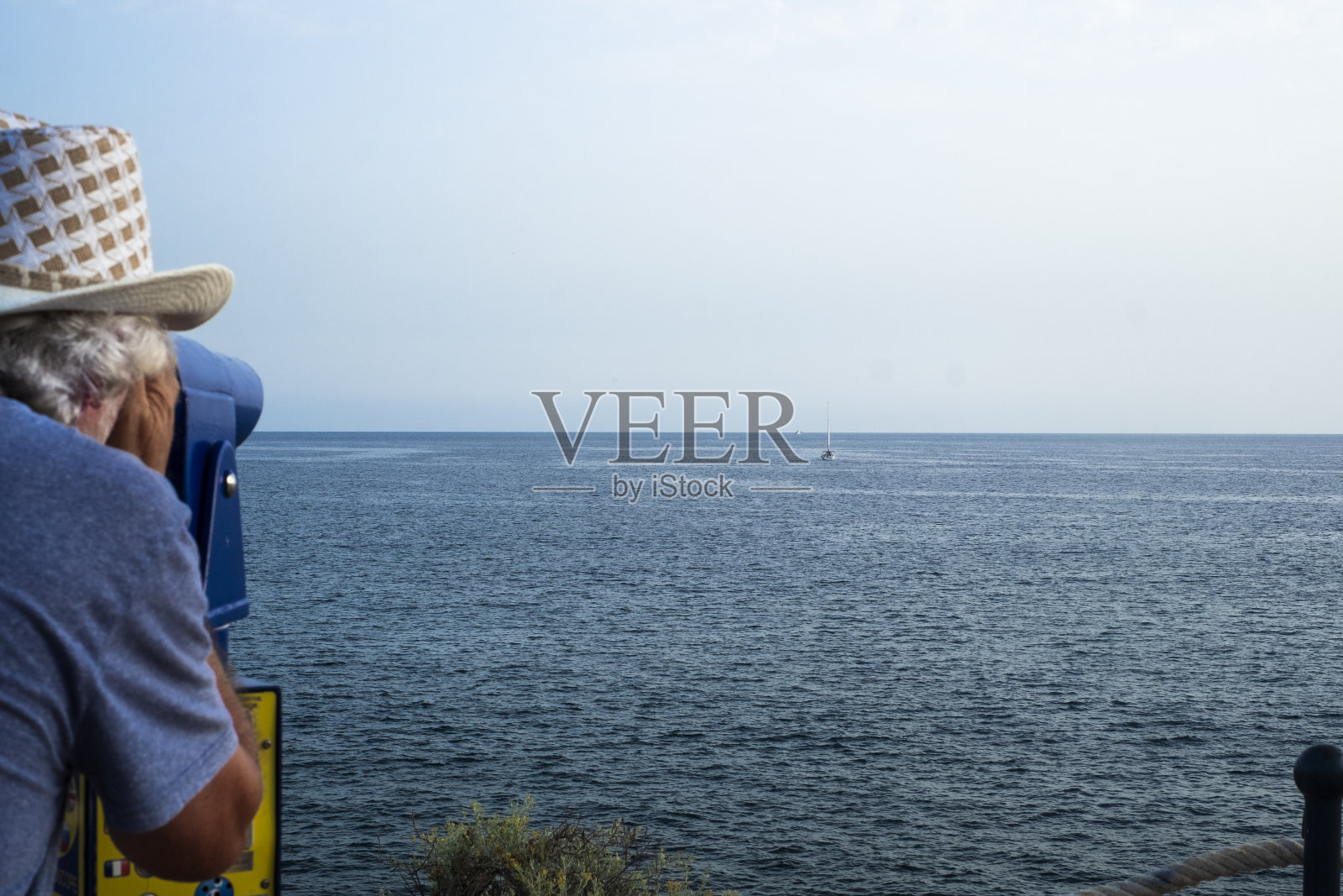 一位老人透过旅游望远镜望向地平线。蓝色的大西洋海景。用于景观探索的投币双筒望远镜照片摄影图片