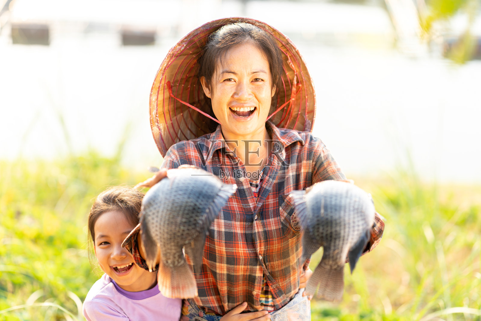 母女俩炫耀着在湄公河上漂浮的篮子里养的大罗非鱼。渔民在商业渔场喂鱼。泰国东北部喂养鱼的罗非鱼。照片摄影图片