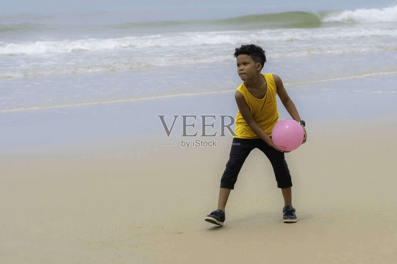 非裔美国男孩在黄色背心玩粉红色的球在海滩上照片摄影图片
