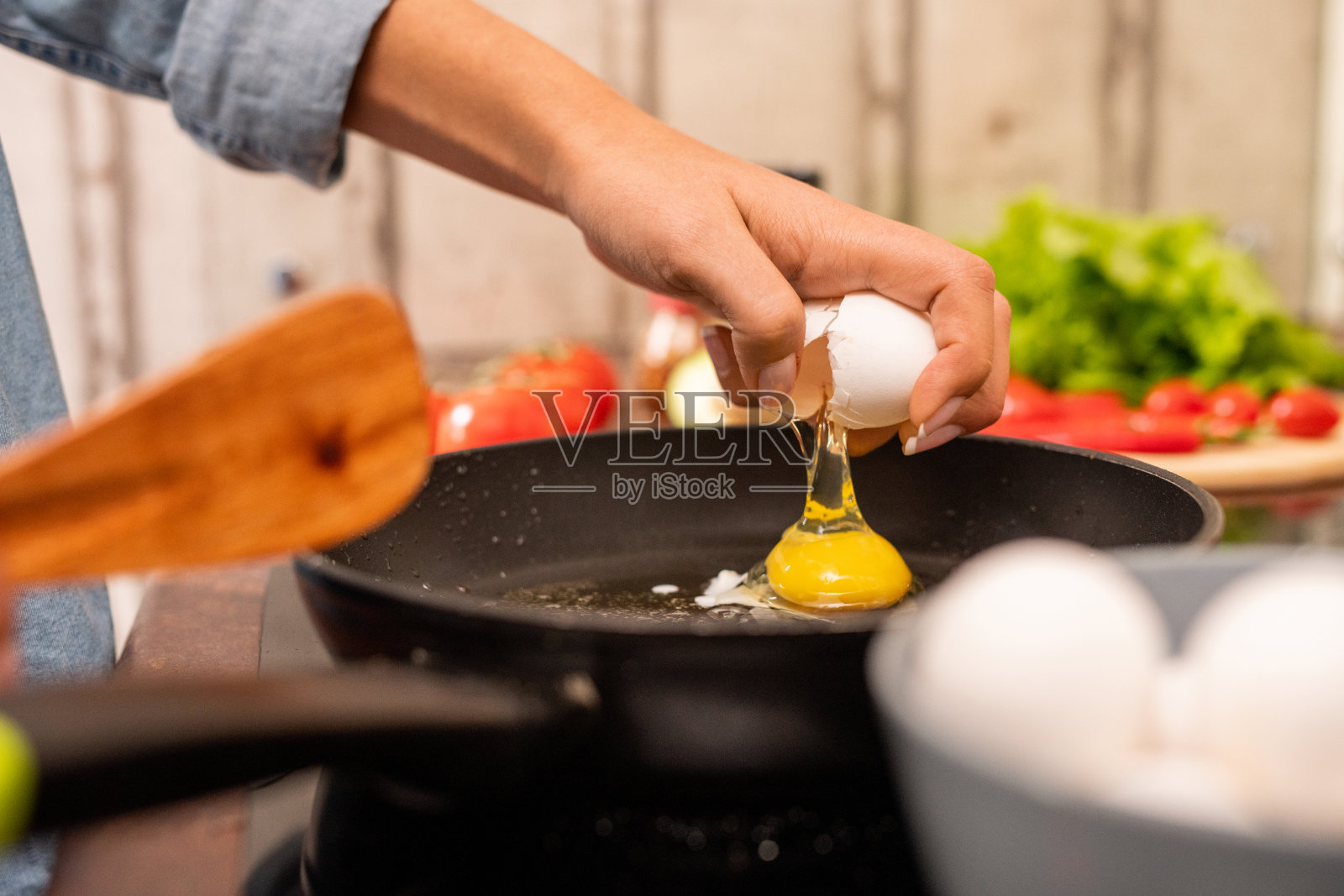 站在电炉上，年轻女子的手在煎锅上打破新鲜的鸡蛋照片摄影图片