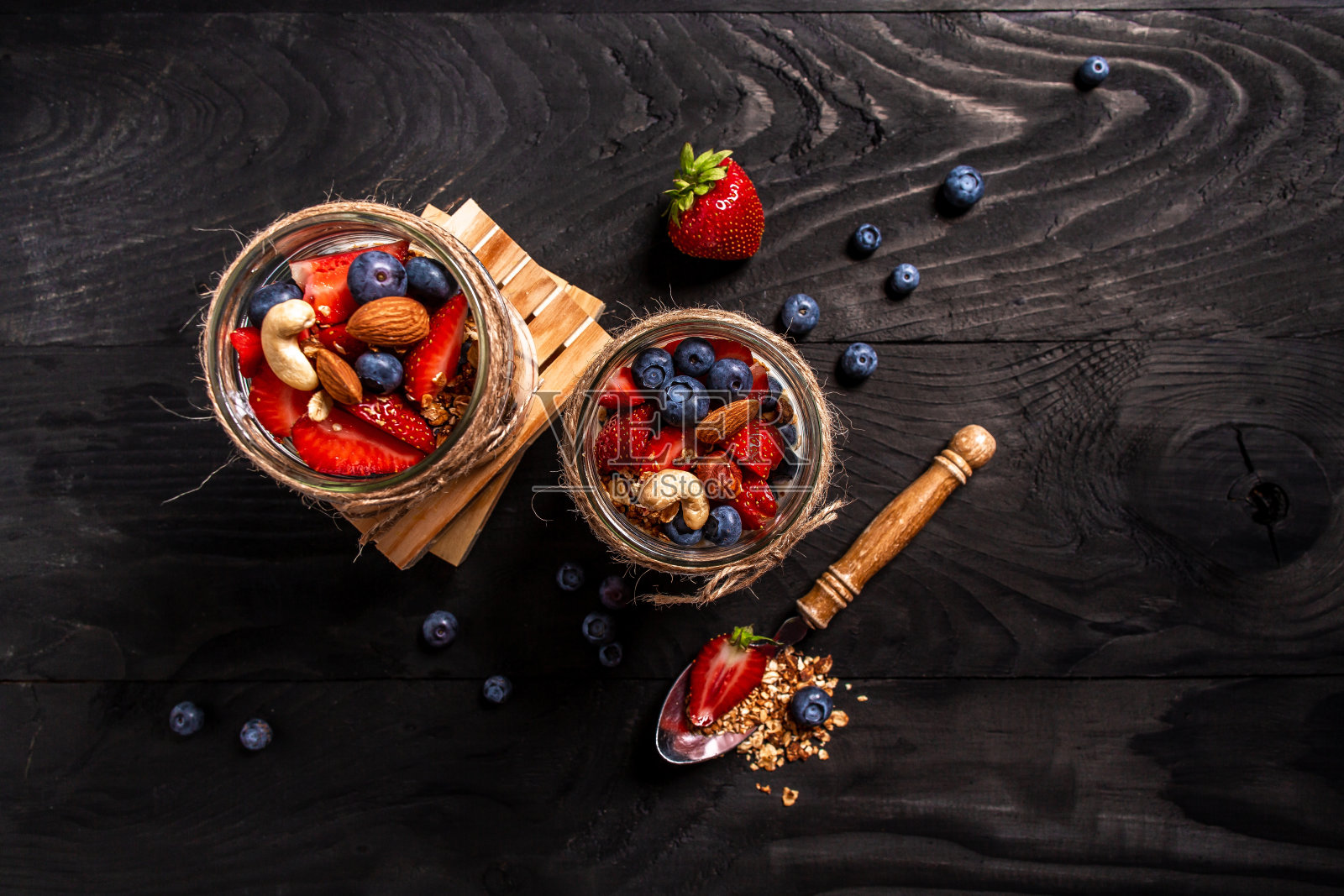 两罐美味的冻糕由格兰诺拉麦片，浆果，坚果和酸奶在木制背景。横幅菜单食谱的文本位置，俯视图照片摄影图片