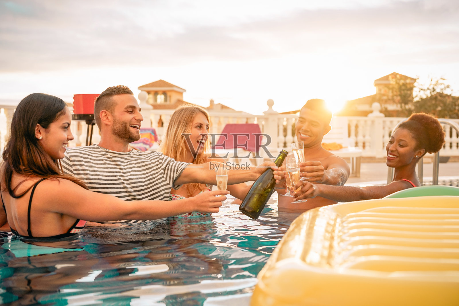 快乐的朋友在泳池派对上敬酒香槟-年轻人有乐趣的喝起泡酒在豪华的热带度假日落-夏季假期和度假青年的生活方式概念照片摄影图片