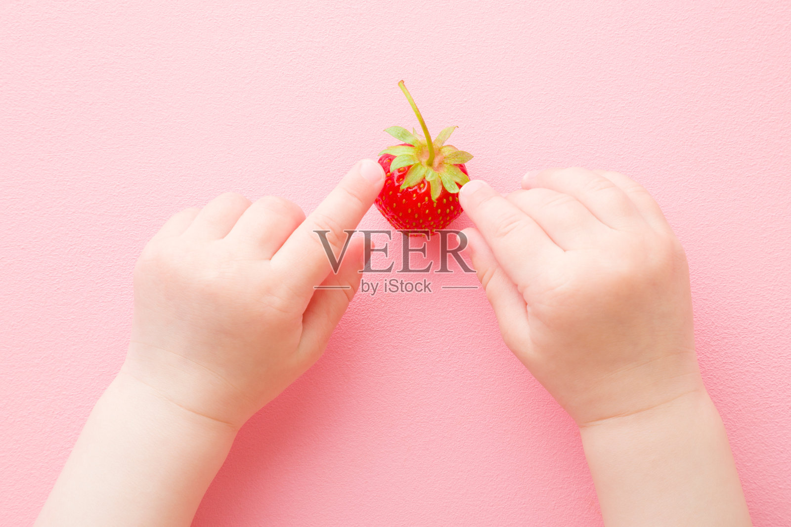 婴儿的手指触摸和探索一个红色的草莓在浅粉色的桌子背景。新鲜的浆果。柔和的颜色。特写镜头。视角拍摄。自顶向下的观点。照片摄影图片