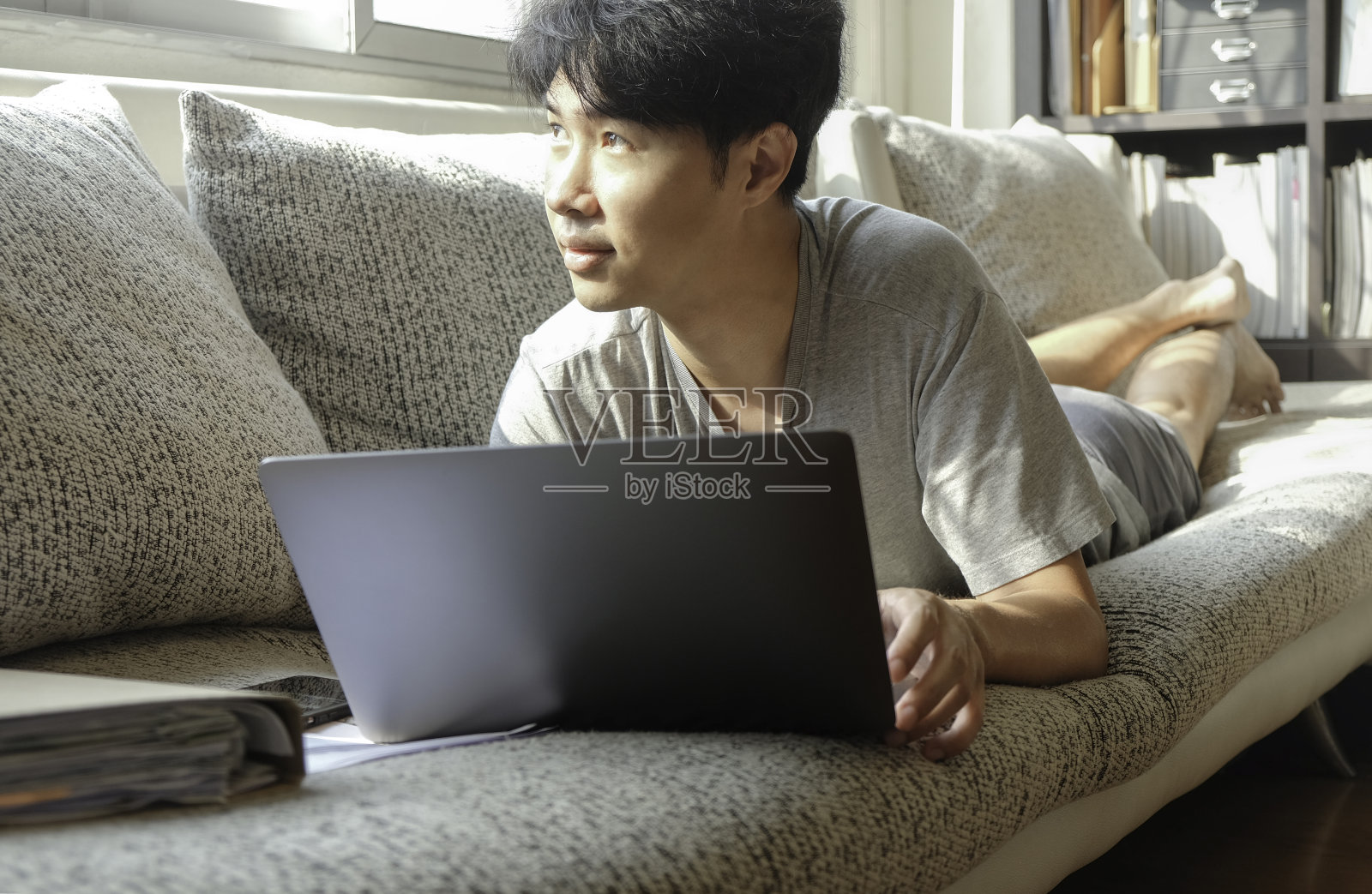 年轻的亚洲男人在沙发上用笔记本电脑从家里工作照片摄影图片