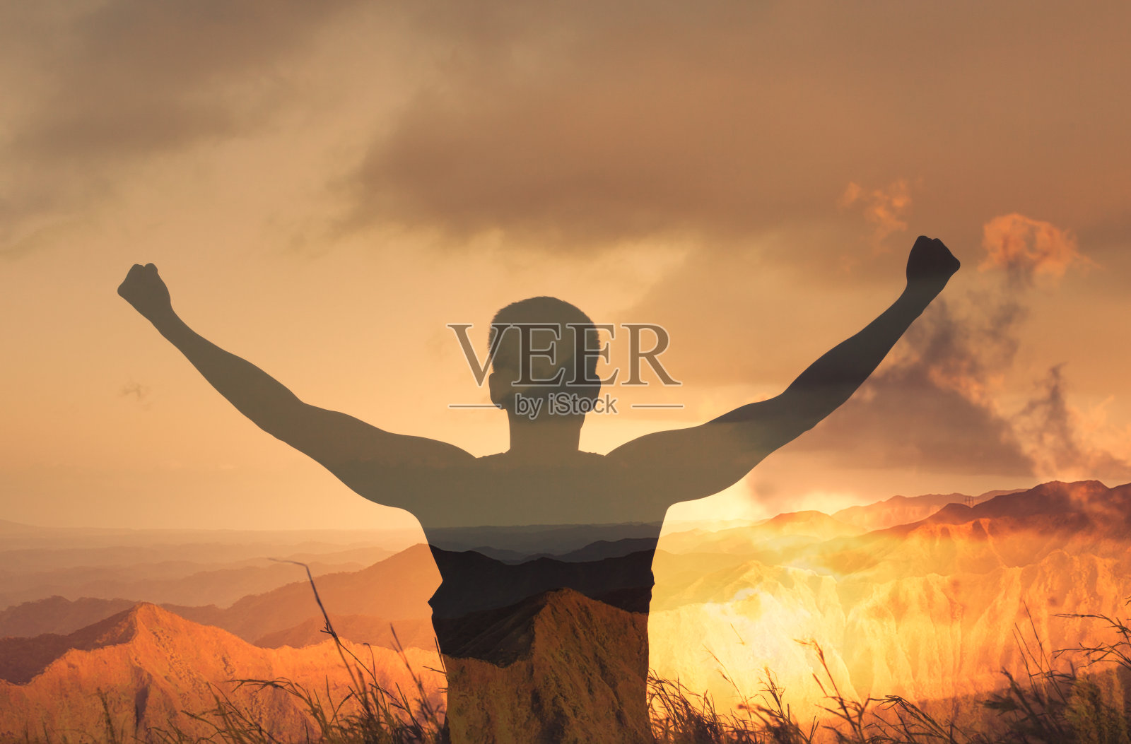一个斗志昂扬的年轻人在山上举起拳头。照片摄影图片